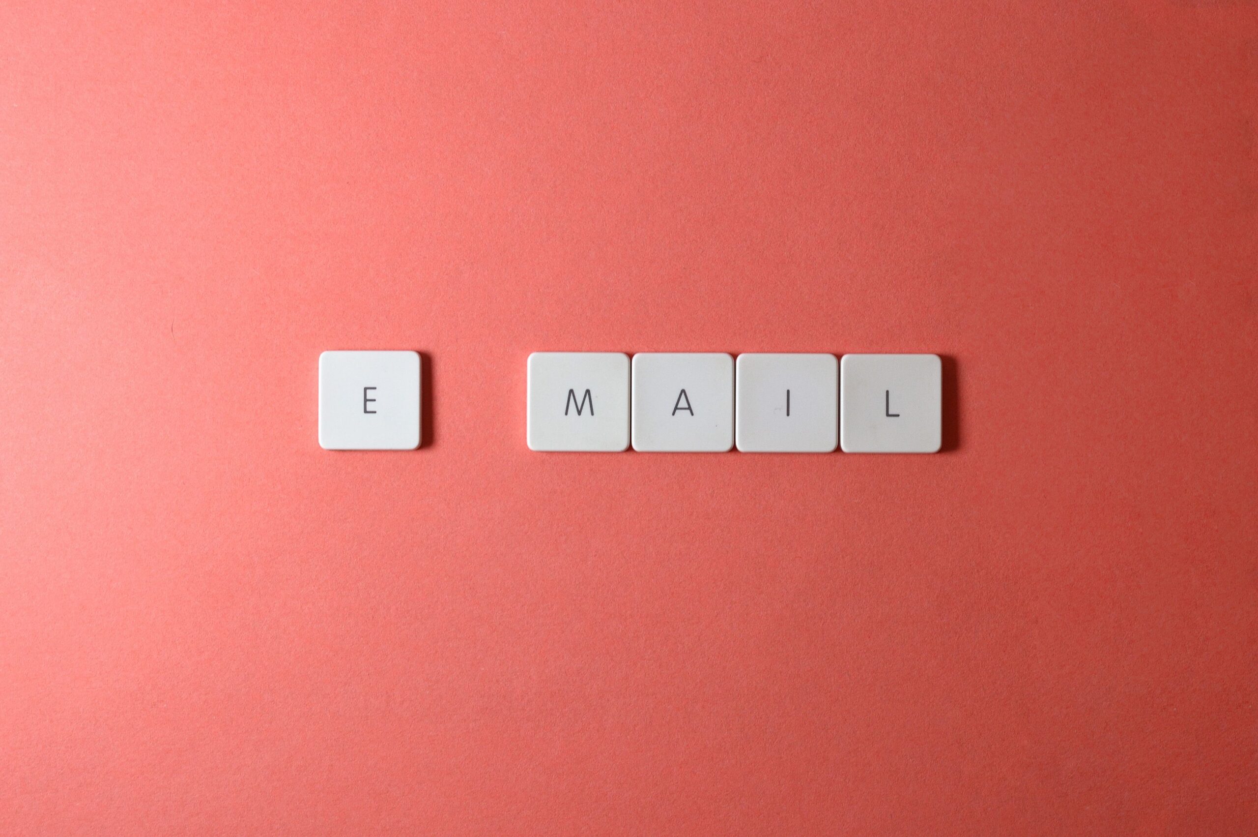Home Flat lay of keyboard letter tiles spelling 'email' on coral backdrop.